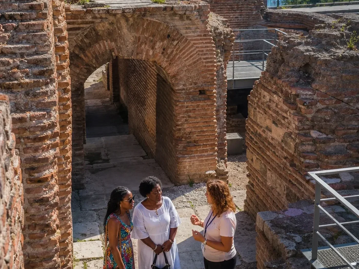 Visitors explore the Roman Baths of Varna with the Black Sea visible beyond the brick ruins.